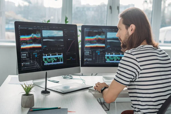 Handsome editor sitting and working near computer monitors — Stock Photo