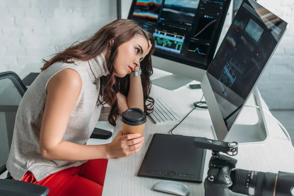 Editor de arte descontente segurando copo de papel e olhando para monitor de computador — Fotografia de Stock