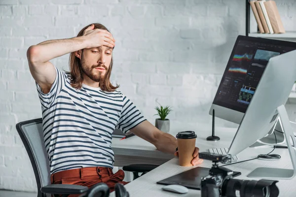 Müder Redakteur hält Pappbecher in der Nähe von Computermonitoren — Stockfoto