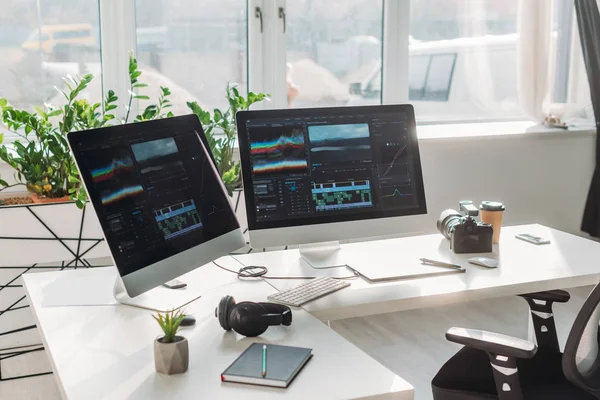 Monitores de computadora con guion gráfico cerca de auriculares y taza de papel en la mesa - foto de stock