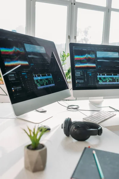 Enfoque selectivo de los monitores de ordenador cerca de los auriculares y la planta en la mesa - foto de stock