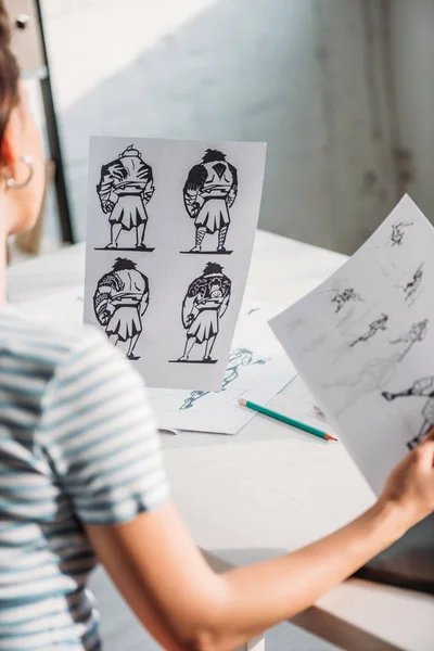 Selective focus of illustrator holding papers with sketches — Stock Photo