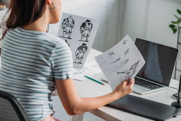 Cropped view of illustrator holding papers with sketches — Stock Photo