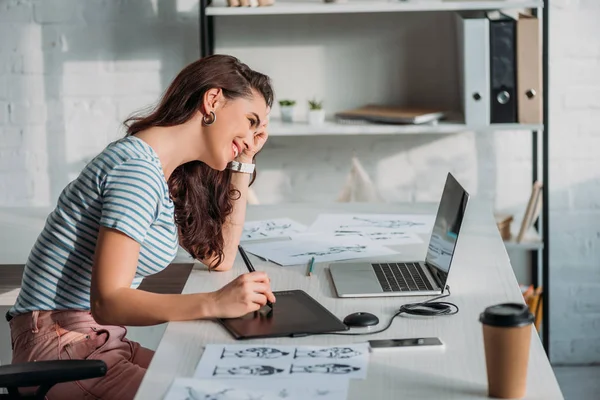 Side view of happy animator using digital tablet near sketches — Stock Photo