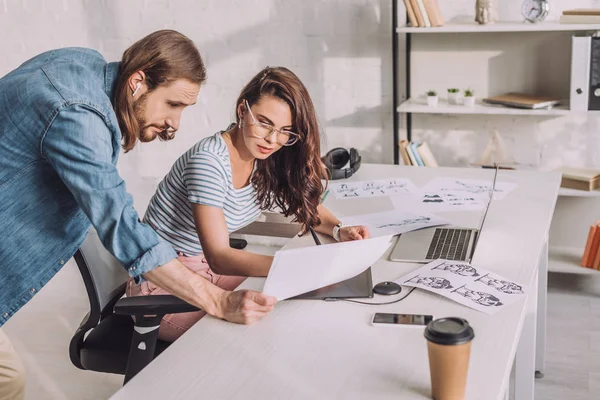 Ilustrador sosteniendo boceto cerca de compañero de trabajo en gafas - foto de stock