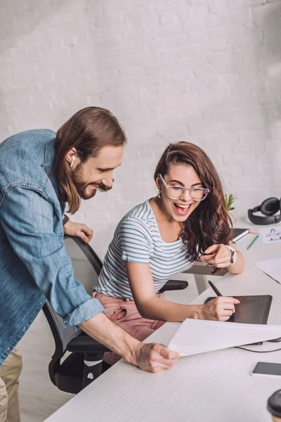 Happy illustrator pointing with finger at sketch near cheerful man — Stock Photo