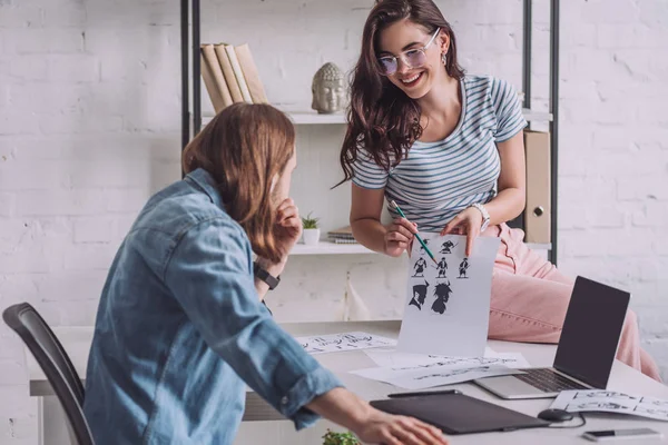 Selektiver Fokus des glücklichen Illustrators, der Cartoon-Skizzen in der Nähe des Menschen hält — Stockfoto