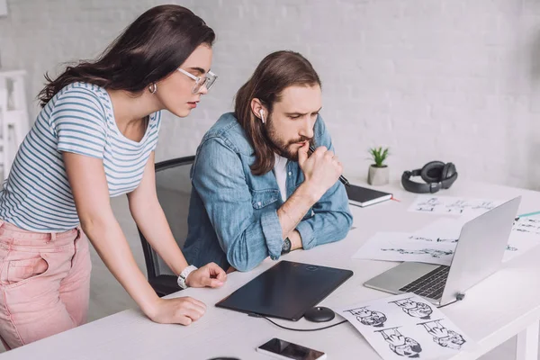 Animators looking at laptop near sketches on table — Stock Photo