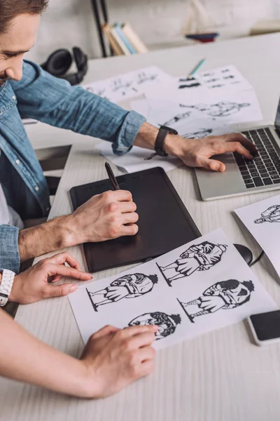 Vue recadrée de l'animateur pointant avec le doigt à dessin animé croquis près de collègue — Photo de stock