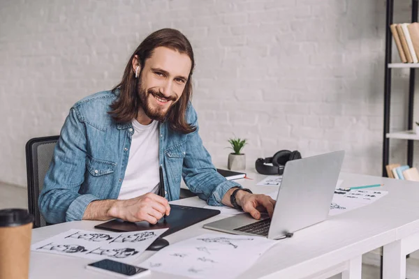 Selective focus of happy animator near gadgets and sketches — Stock Photo