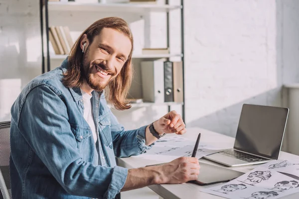 Heureux animateur dans les écouteurs sans fil près des croquis et des gadgets — Photo de stock