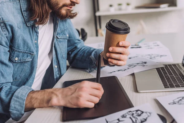 Vue recadrée de l'animateur barbu tenant une tasse en papier près des croquis — Photo de stock