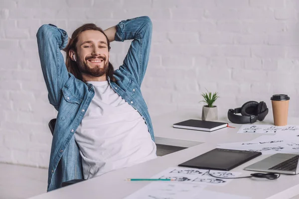 Cheerful illustrator in wireless earphones near sketches on table — Stock Photo