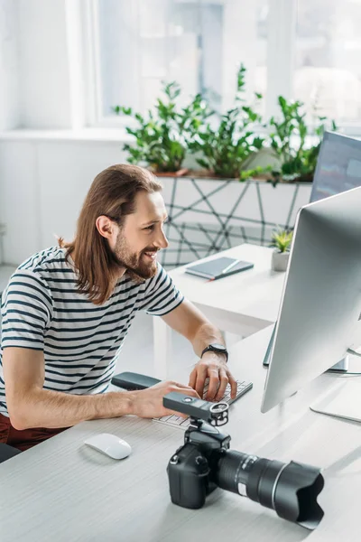 Éditeur heureux et barbu travaillant près de l'appareil photo numérique en studio — Photo de stock