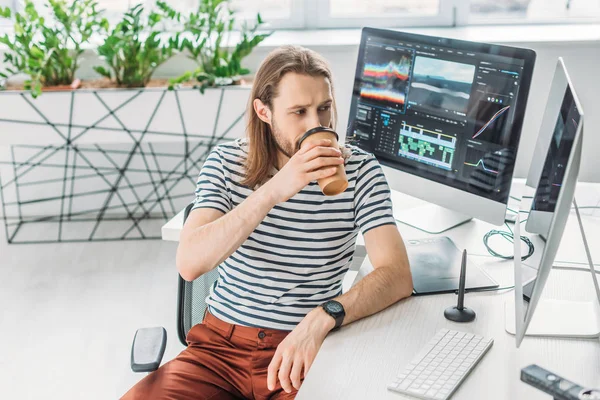 Editor de arte mirando el monitor de la computadora mientras bebe café para ir - foto de stock