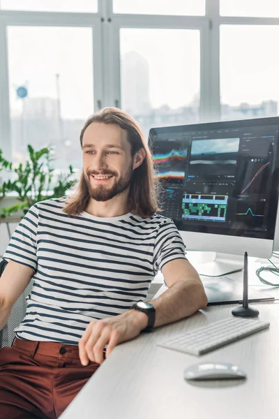 Selektiver Fokus des bärtigen Redakteurs, der in der Nähe des Computermonitors wegschaut — Stockfoto