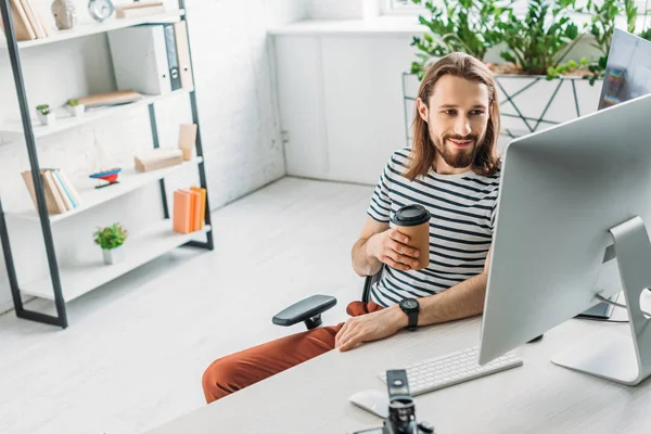 Glücklicher Kunstredakteur blickt auf Computermonitor und hält Pappbecher in der Hand — Stockfoto