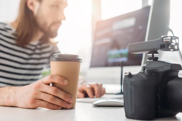 Foco seletivo do editor segurando copo de papel e olhando para o monitor do computador — Fotografia de Stock