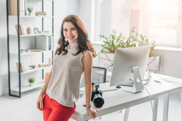 Belo editor de arte sorrindo perto de câmera digital e monitor de computador — Fotografia de Stock