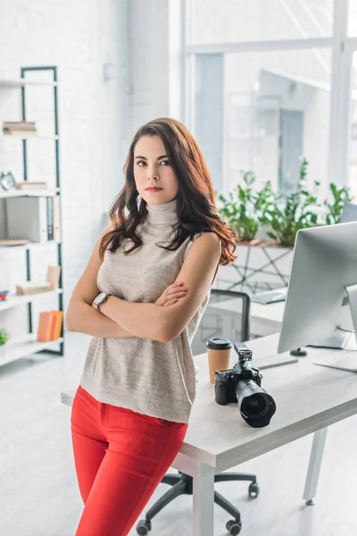 Beautiful art editor standing with crossed arms near digital camera and computer monitor — Stock Photo