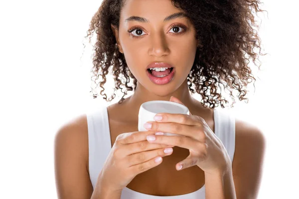 Encaracolado surpreendido menina americana africana segurando recipiente de plástico com creme facial, isolado em branco — Fotografia de Stock