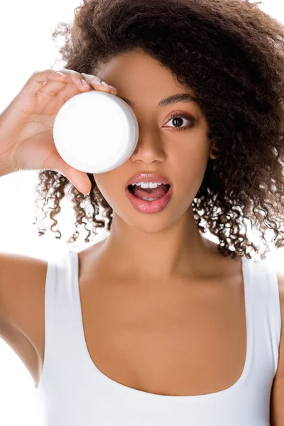 Menina afro-americana surpreso segurando recipiente de plástico com creme facial, isolado em branco — Fotografia de Stock
