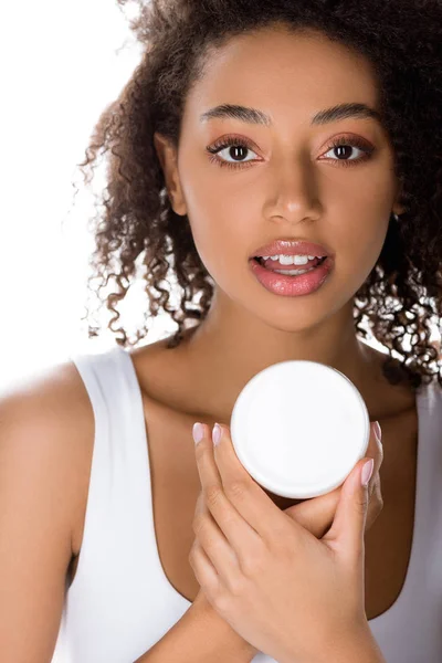 Encaracolado menina americana africana segurando recipiente de plástico com creme facial, isolado em branco — Fotografia de Stock