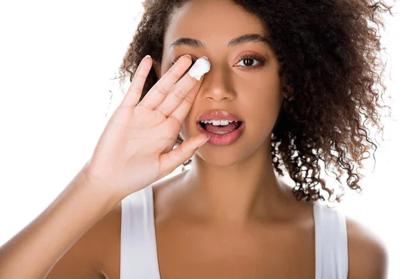 Hermosa chica afroamericana con frenos dentales aplicando crema hidratante, aislado en blanco - foto de stock