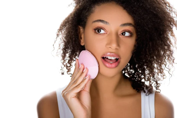 Scioccato ragazza afroamericana utilizzando spazzola viso detergente in silicone, isolato su bianco — Foto stock