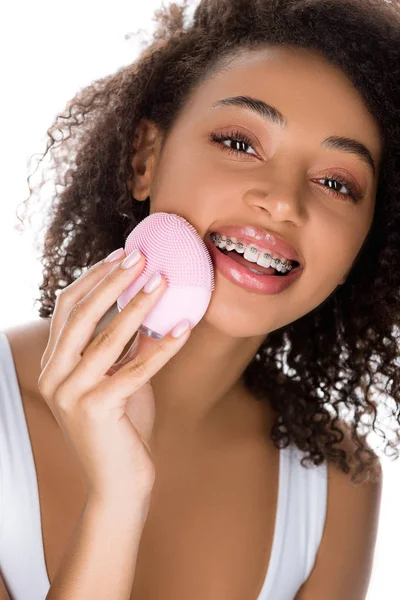 Menina americana africana feliz com aparelho dentário usando escova facial de limpeza de silicone, isolado em branco — Fotografia de Stock