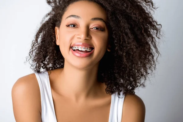 Riéndose chica afroamericana con frenos dentales, aislado en gris - foto de stock