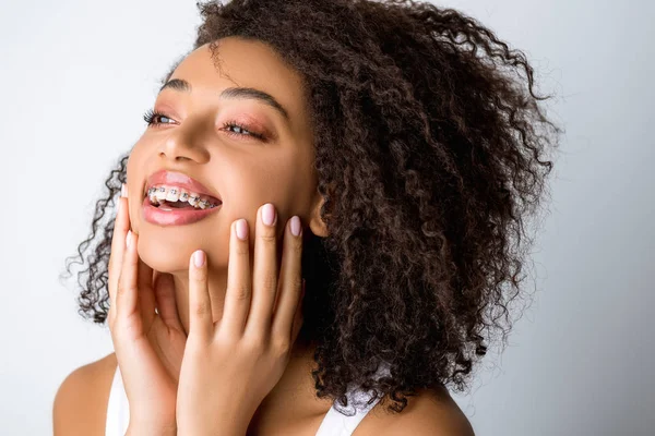 Hermosa riéndose chica afroamericana con frenos dentales, aislado en gris - foto de stock