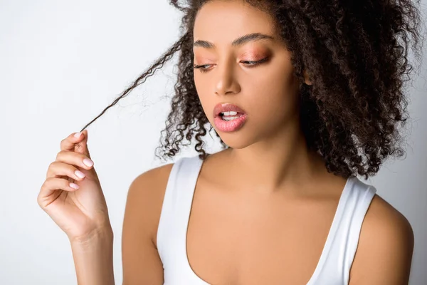 Ritratto di una ragazza afroamericana preoccupata che guarda i suoi capelli ricci, isolata sul grigio — Foto stock