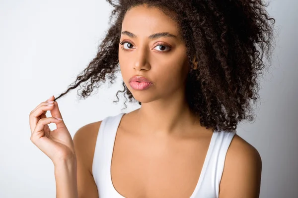 Retrato de chica afroamericana sosteniendo su cabello rizado, aislado en gris - foto de stock