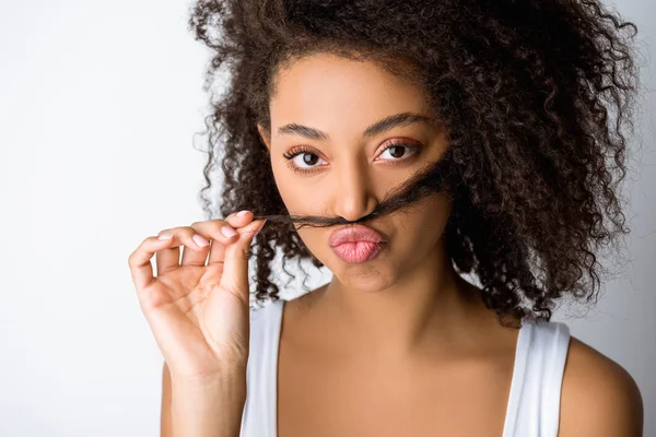Portrait d'une drôle de fille afro-américaine faisant une fausse moustache à partir de cheveux, isolée sur gris — Photo de stock