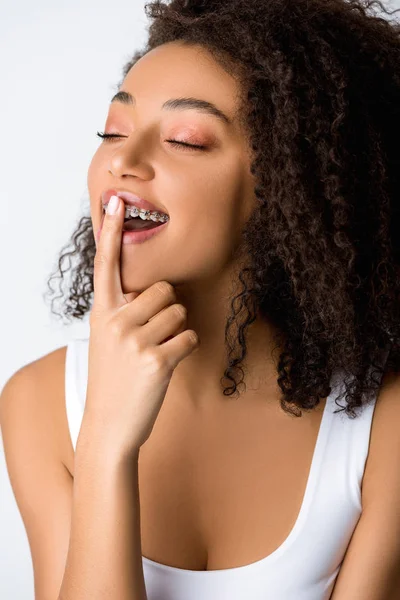 Chica afroamericana soñadora con frenos dentales, aislada en gris - foto de stock