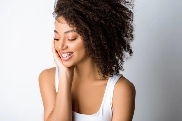 Souriant frisé afro-américain fille avec des appareils dentaires, isolé sur gris — Photo de stock