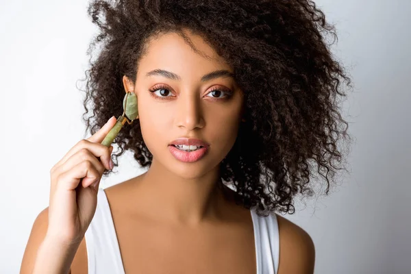 Menina americana africana atraente usando rolo facial de pedra, isolado em cinza — Fotografia de Stock