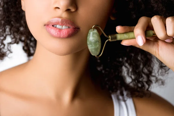 Cropped view of african american girl using stone facial roller, isolated on grey — Stock Photo