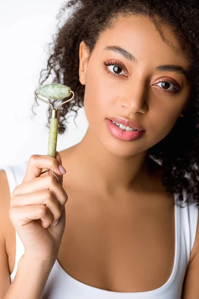 Beautiful african american girl holding jade facial roller, isolated on grey — Stock Photo