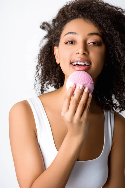 Happy african american woman with braces using silicone cleansing facial brush, isolated on grey — Stock Photo