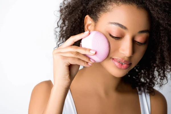 Chica afroamericana sonriente con los ojos cerrados usando cepillo facial limpiador de silicona, aislado en gris — Stock Photo