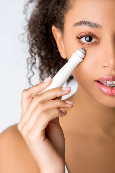 Curly african american girl using moisturizing eye roller, isolated on grey — Stock Photo