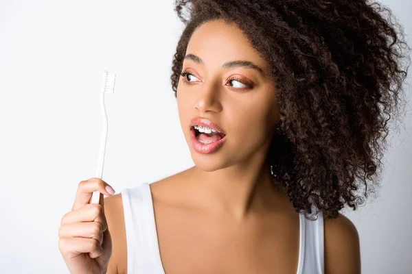Surprised african american woman with dental braces looking at toothbrush, isolated on grey — Stock Photo