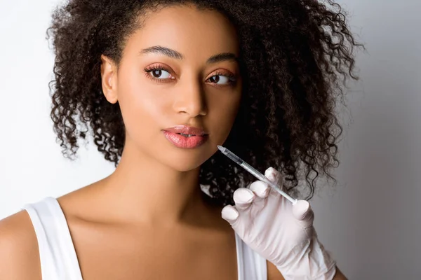 Mujer afroamericana joven haciendo inyección de belleza, aislada en gris - foto de stock