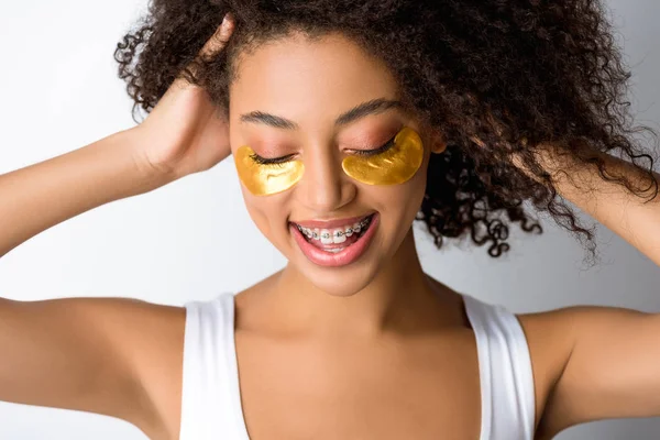 Sorridente menina afro-americana com manchas olho dourado e aparelho, isolado em cinza — Fotografia de Stock