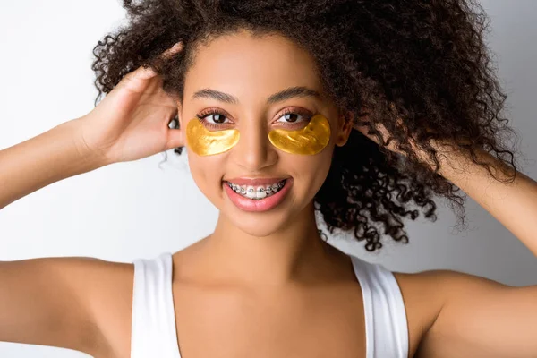 Menina americana africana alegre com manchas olho dourado e aparelho dentário, isolado em cinza — Fotografia de Stock