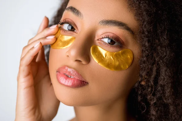 Привлекательная брюнетка африканская американка с золотыми повязками на глазу, изолированная на сером — стоковое фото