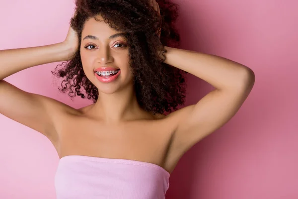 Felice ragazza afroamericana riccia con bretelle dentali su rosa — Foto stock