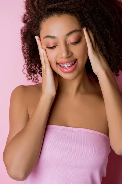 Souriant afro-américain fille avec des appareils dentaires, isolé sur rose — Photo de stock